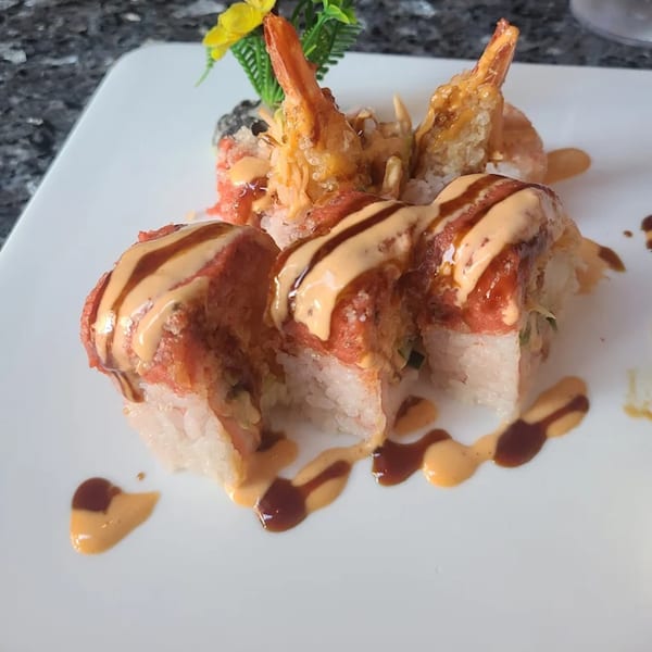 Kabuki Japanese Cuisine's sushi rolls with tempura shrimp and drizzled with two sauces on a white plate.