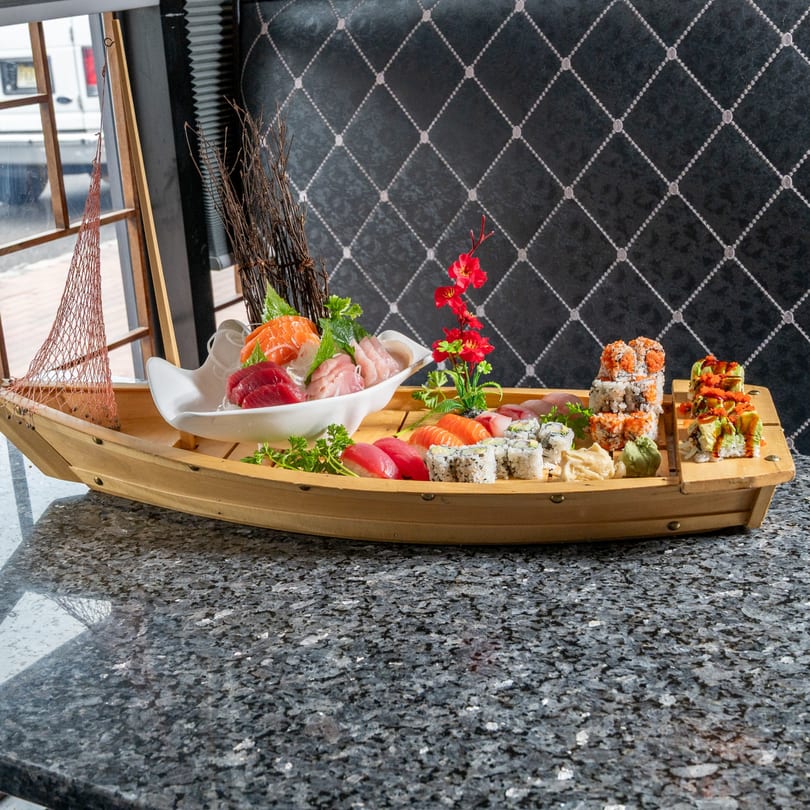 A large wooden boat filled with various sushi, sashimi, and rolls on a granite table.