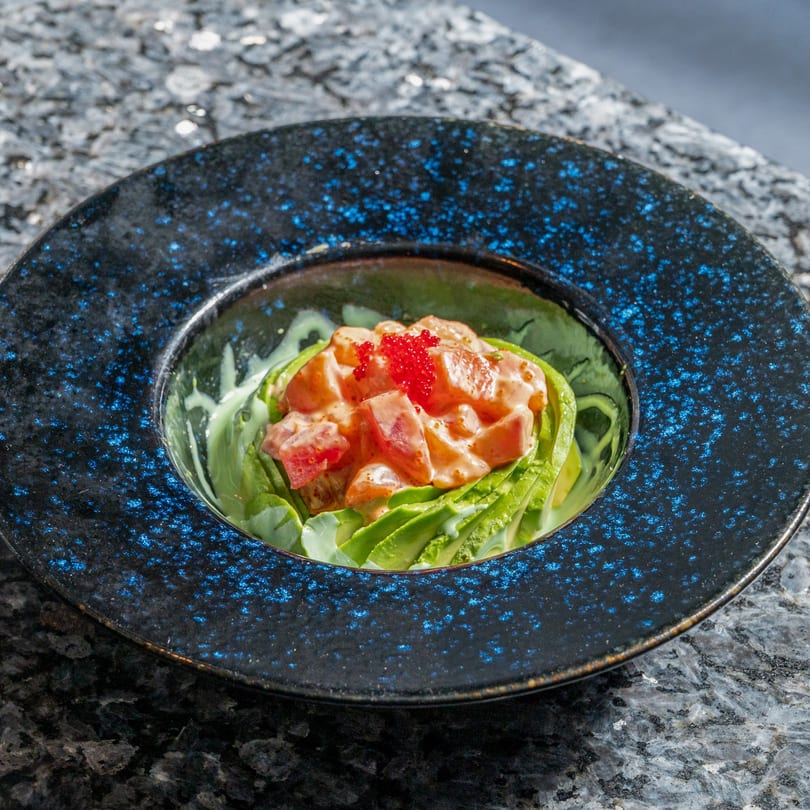 Kabuki Japanese Cuisine's salmon poke with avocado and red roe in a blue speckled bowl.