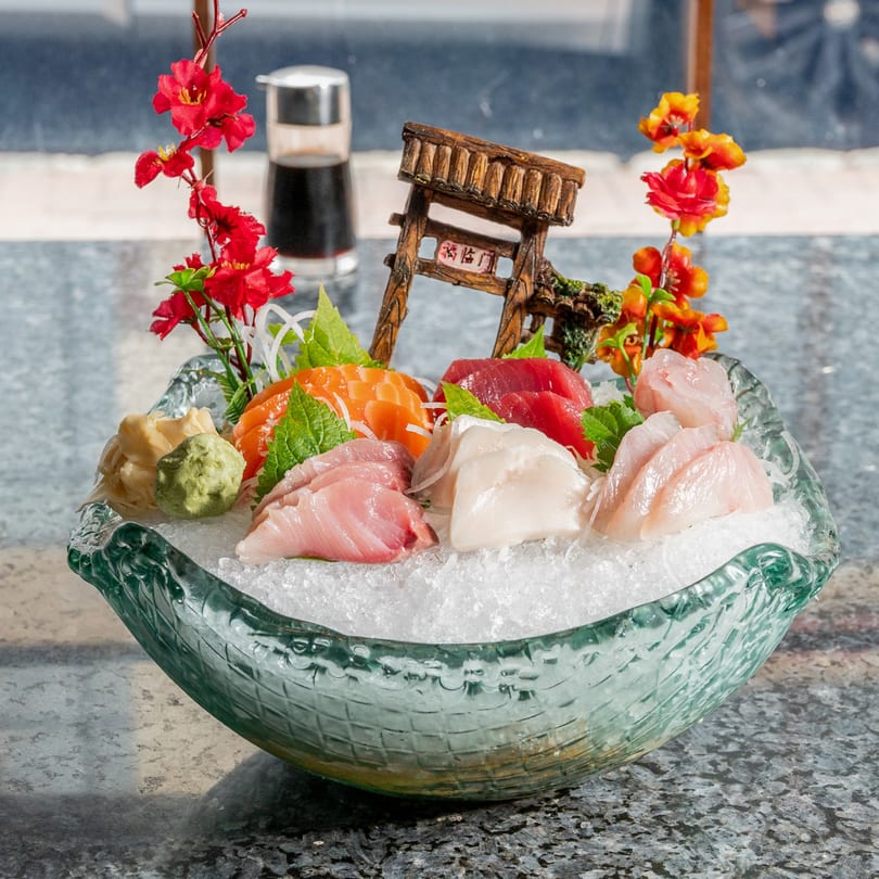 Assorted sashimi, including salmon, tuna, and white fish, served on ice in a decorative glass bowl.