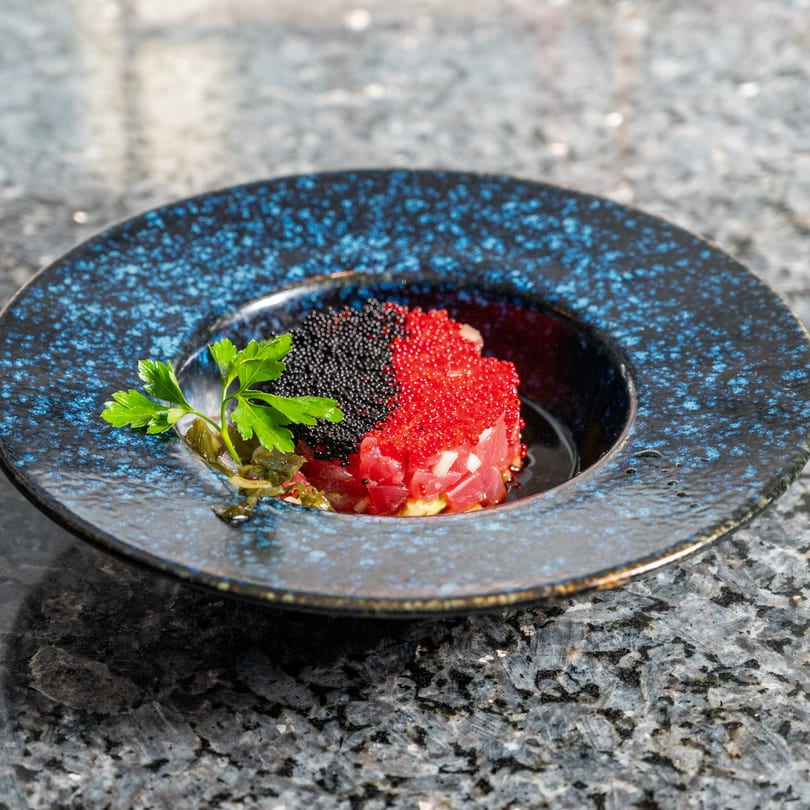 Kabuki Japanese Cuisine's tuna tartare with black and red caviar, garnished with parsley in a blue bowl.